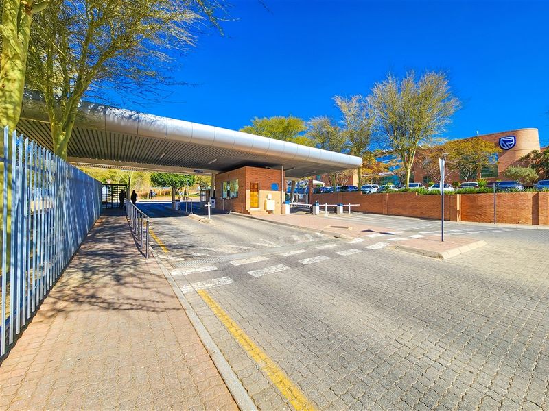 A professional view of the office park entrance featuring a secure boom gate, guard house, and paved driveway access.