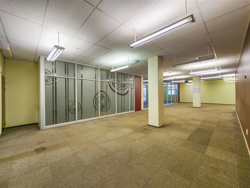 Spacious open-plan office area featuring suspended ceilings, fluorescent lighting, carpeted flooring, and decorative glass partition walls.
