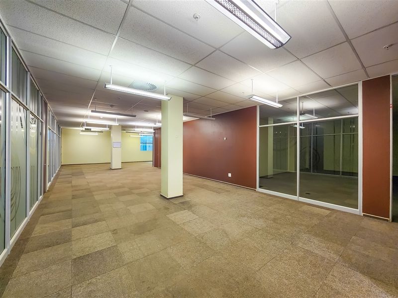 Spacious open-plan office area featuring suspended ceilings, glass partitioning, and carpeted flooring, offering a versatile layout for professional use.