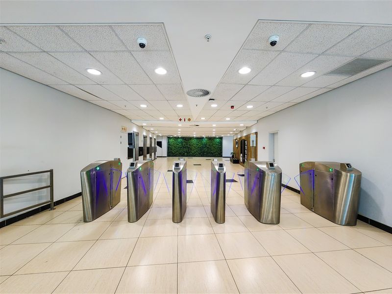 Modern office building entrance lobby featuring stainless steel security turnstiles, tiled flooring, and a decorative vertical garden wall.