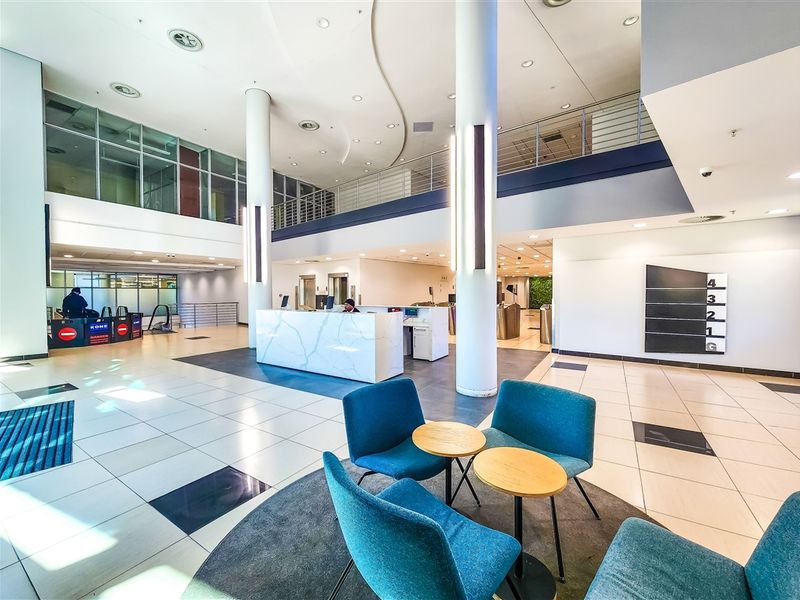 Spacious modern office building lobby featuring a marble-finish reception desk, high ceilings with mezzanine level, and secure elevator access.
