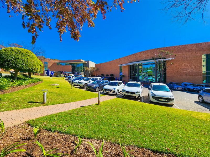 A well-maintained office building exterior featuring a brick facade, large glass windows, and a landscaped parking area with paved walkways.