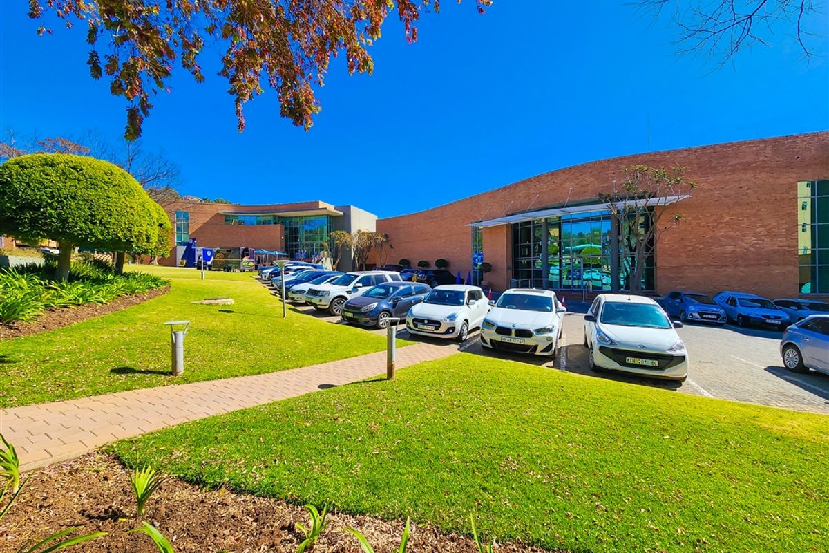 A well-maintained office building exterior featuring a brick facade, large glass windows, and a landscaped parking area with paved walkways.