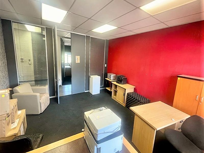 A functional office space featuring a suspended ceiling, recessed lighting, and a glass partition wall, currently showing signs of wear on the walls and carpet.