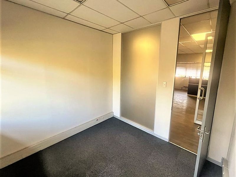 An empty office space featuring a suspended ceiling, carpeted flooring, and a frosted glass partition with a glass door.