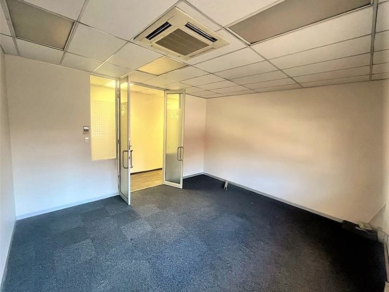 A vacant office space featuring a suspended ceiling with integrated air conditioning, carpet tile flooring, and glass partition doors.