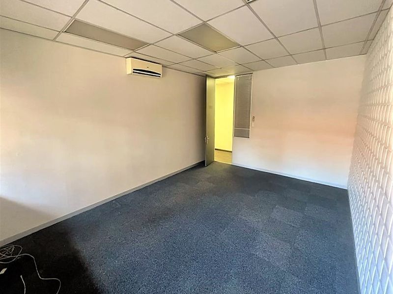 A vacant office space featuring carpet tiles, a suspended ceiling, and a wall-mounted split-system air conditioning unit.