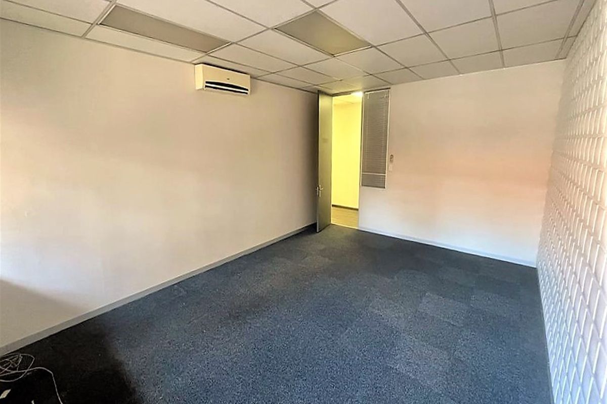 A vacant office space featuring carpet tiles, a suspended ceiling, and a wall-mounted split-system air conditioning unit.
