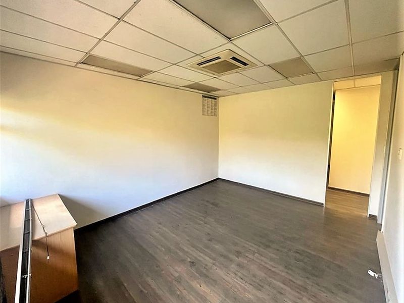 An empty office space featuring laminate flooring, a suspended ceiling with integrated lighting, and a central air conditioning unit.