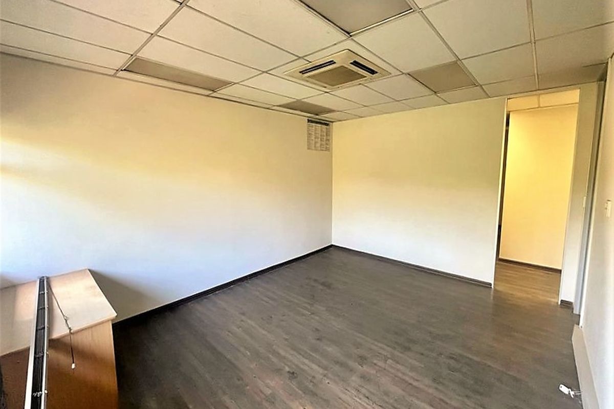 An empty office space featuring laminate flooring, a suspended ceiling with integrated lighting, and a central air conditioning unit.