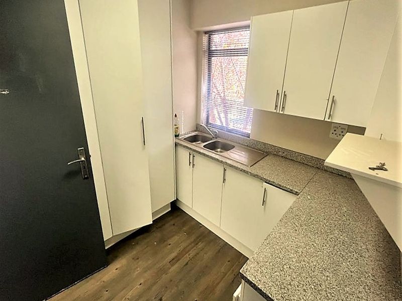 A compact, functional kitchenette featuring white built-in cabinetry, granite-look laminate countertops, a stainless steel double sink, and durable wood-look laminate flooring.
