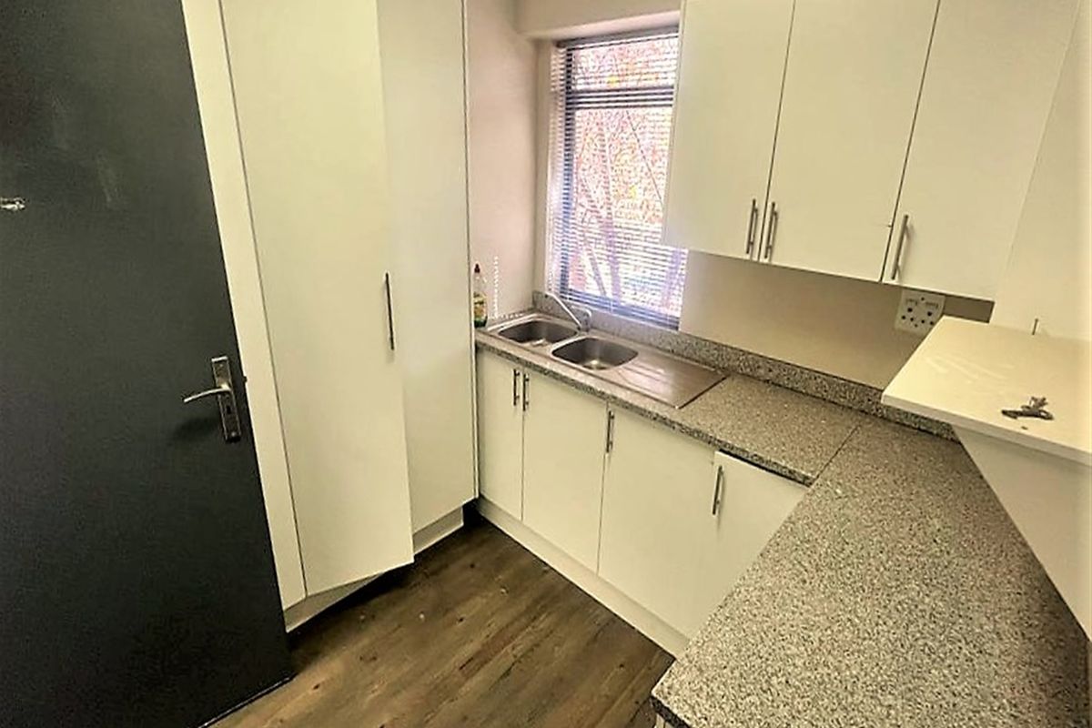 A compact, functional kitchenette featuring white built-in cabinetry, granite-look laminate countertops, a stainless steel double sink, and durable wood-look laminate flooring.
