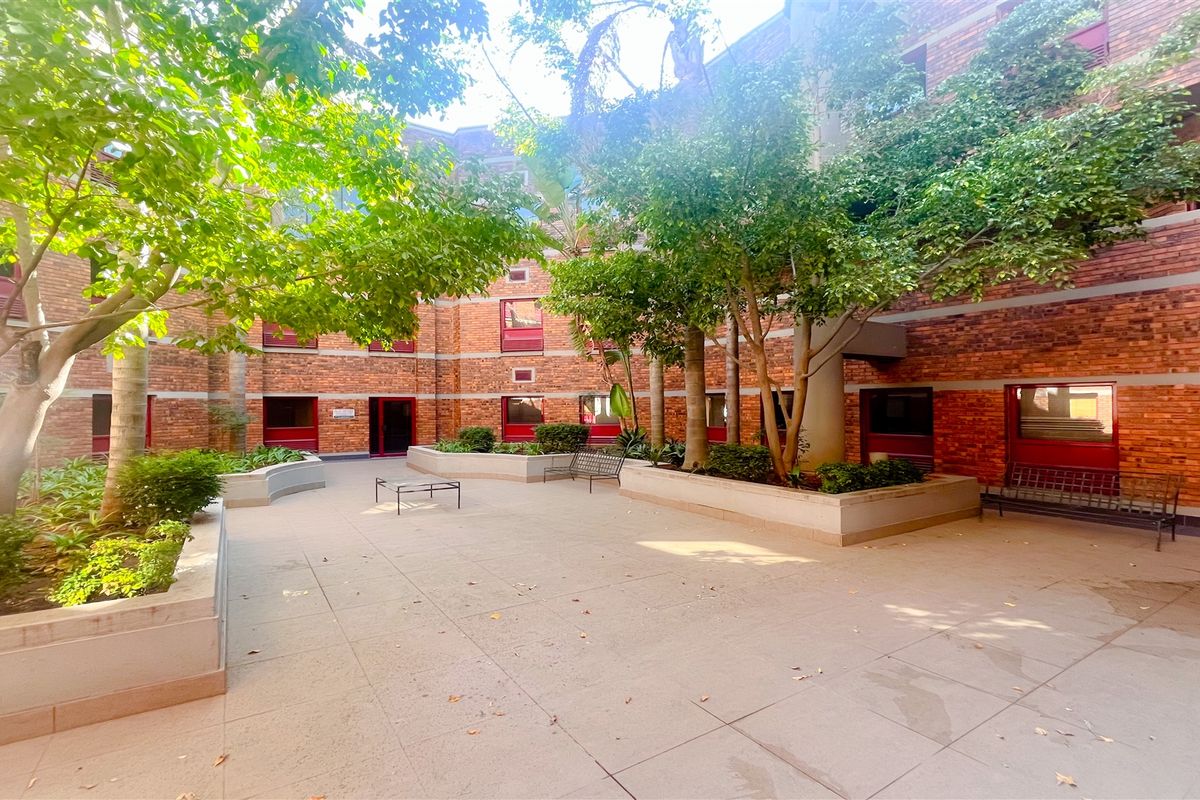 A well-maintained brick office building courtyard featuring paved walkways, raised concrete planters, and mature trees providing a pleasant outdoor space.
