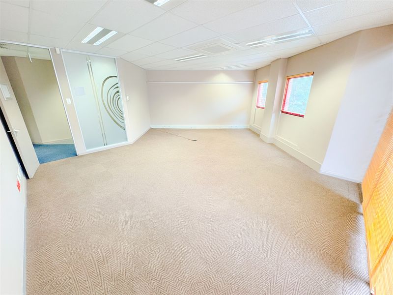 A spacious, empty office suite featuring neutral carpeting, a suspended ceiling with recessed lighting, and a modern frosted glass partition.
