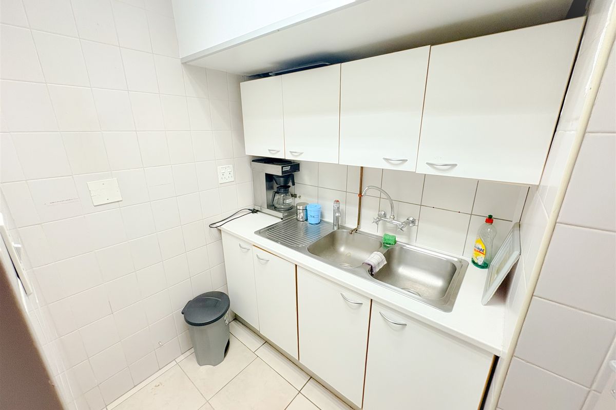 A compact office kitchenette featuring white cabinetry, a double stainless steel sink, and tiled finishes throughout.