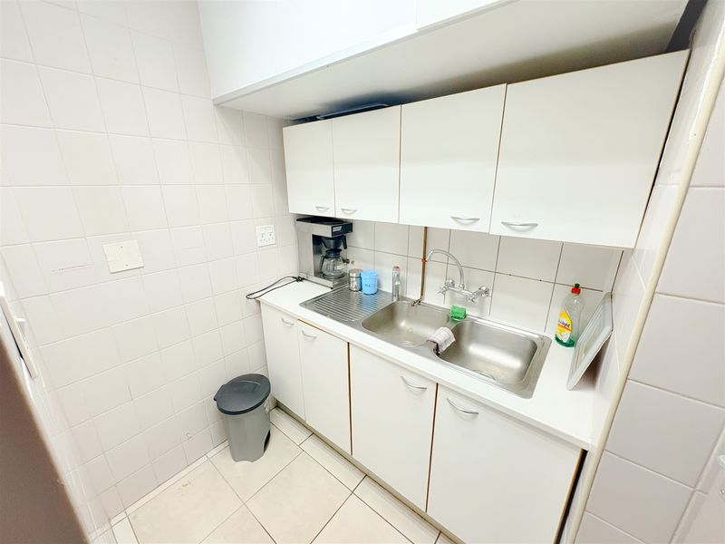 A compact office kitchenette featuring white cabinetry, a double stainless steel sink, and tiled finishes throughout.