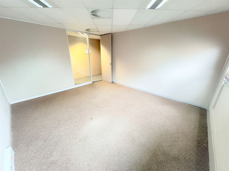A vacant, carpeted office space featuring a suspended ceiling with recessed lighting and a glass partition door.