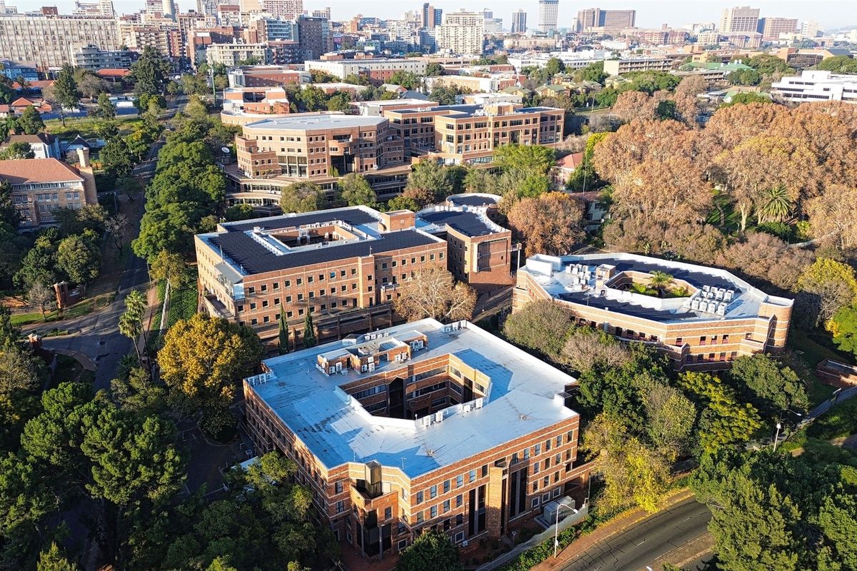 Aerial view of a multi-building office complex featuring brick facades, flat roofs with HVAC installations, and surrounding mature trees in an urban setting.