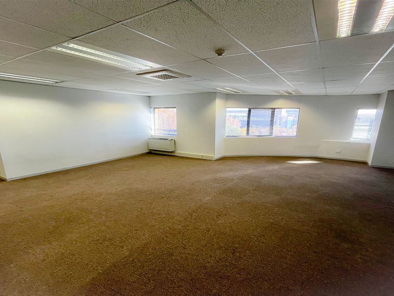 A spacious, empty office suite featuring a suspended ceiling with recessed lighting, HVAC climate control, and large windows providing natural light.