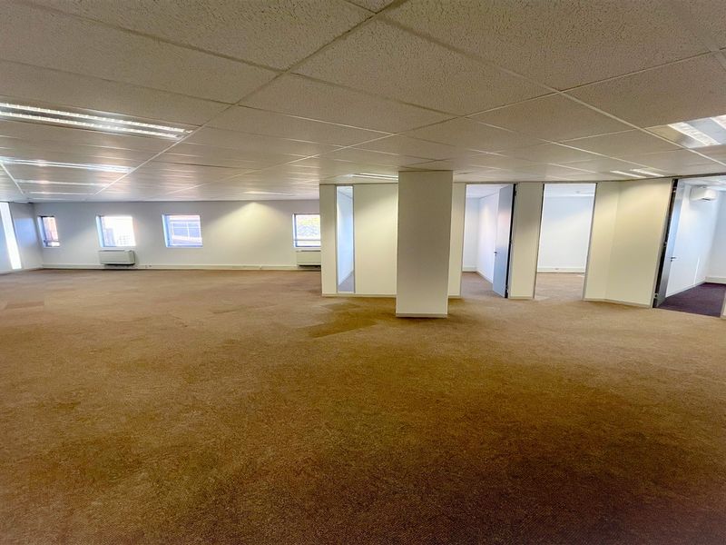 A spacious, open-plan office area featuring suspended ceilings, recessed lighting, and carpeted flooring, offering a versatile layout for various business configurations.