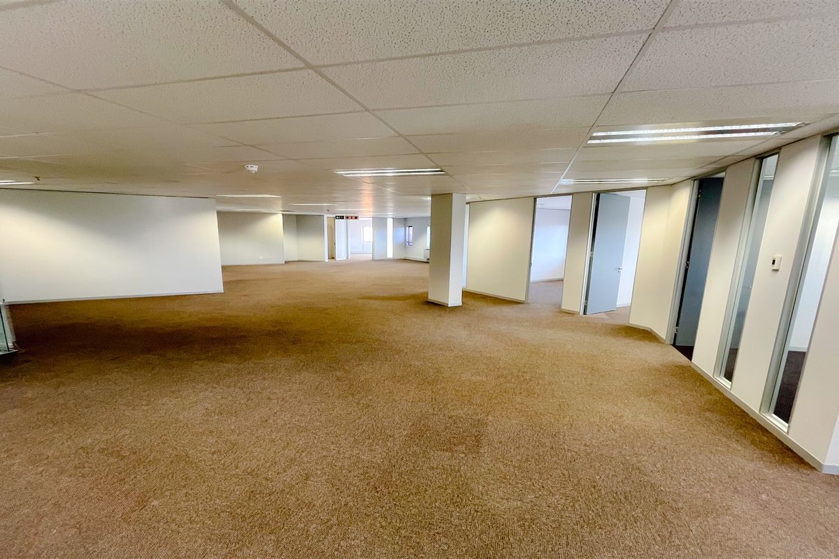 A spacious, open-plan office area featuring neutral carpeting, suspended ceilings with recessed lighting, and glass-partitioned private office spaces.