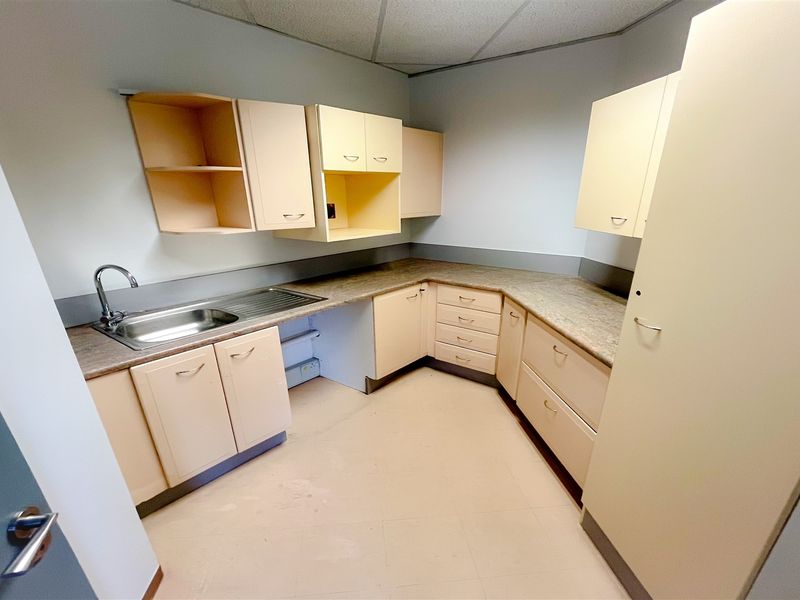 A functional office kitchenette featuring laminate countertops, built-in cabinetry, and a stainless steel sink, offering a practical space for staff amenities.