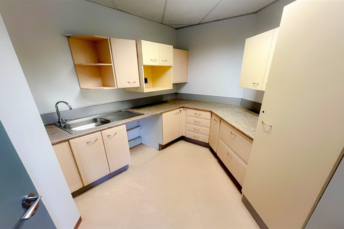 A functional office kitchenette featuring laminate countertops, built-in cabinetry, and a stainless steel sink, offering a practical space for staff amenities.