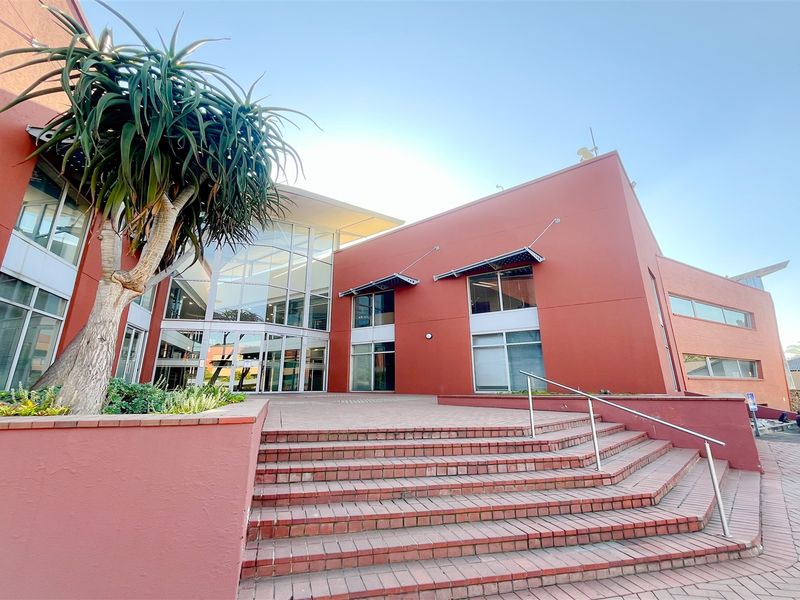 Modern office building entrance featuring a prominent glass facade, brick staircase with metal handrails, and well-maintained exterior finishes.