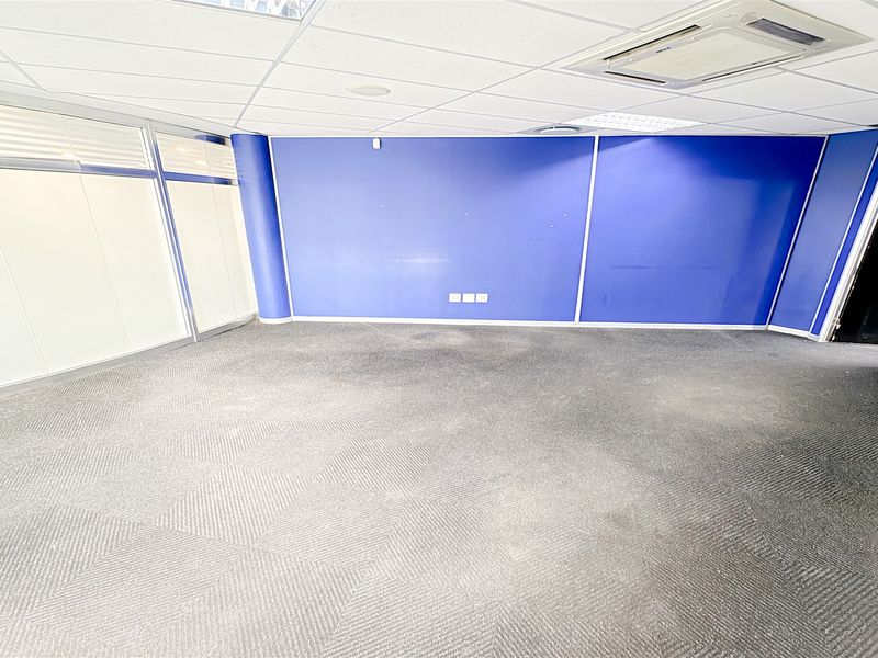 An empty office space featuring a suspended ceiling, ducted air conditioning, glass partitioning, and carpeted flooring.