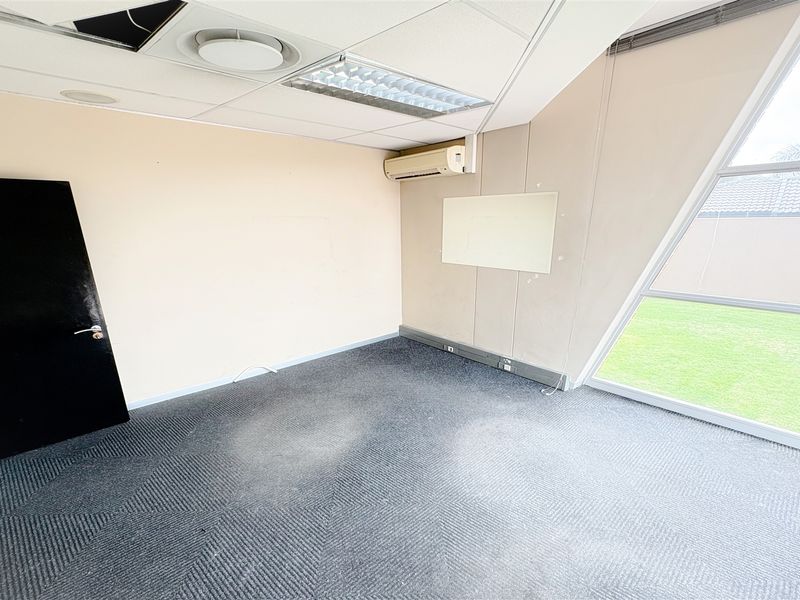 Empty office space featuring a suspended ceiling, split-system air conditioning, carpeted flooring, and a large angled window overlooking the exterior grounds.
