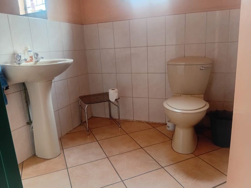 A functional bathroom featuring a pedestal basin and ceramic toilet with neutral wall and floor tiling.