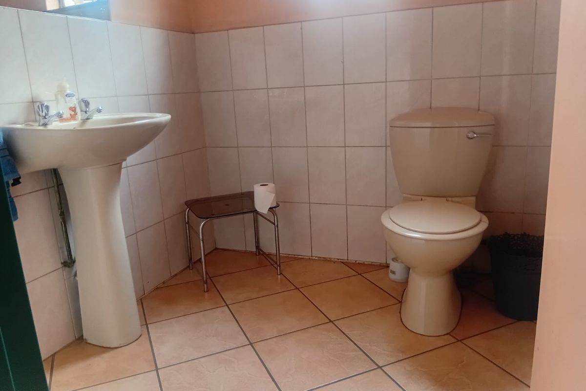 A functional bathroom featuring a pedestal basin and ceramic toilet with neutral wall and floor tiling.
