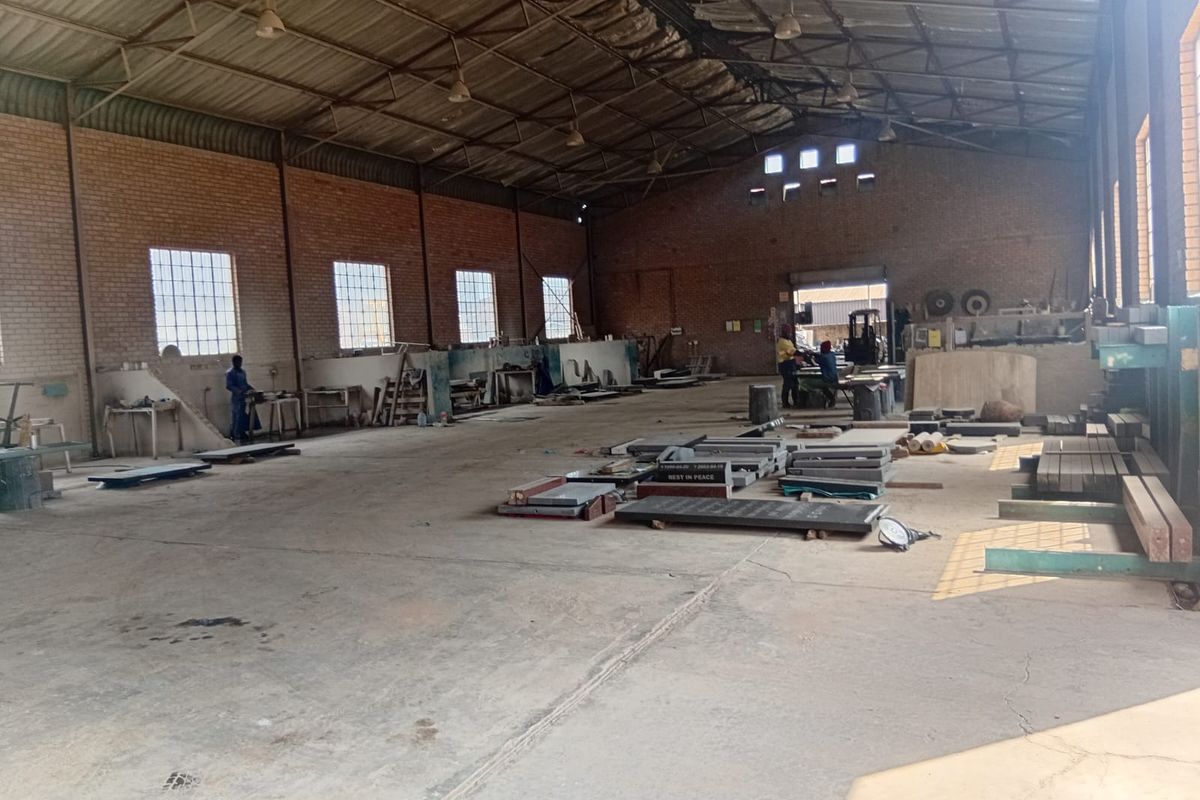 Spacious industrial warehouse featuring exposed brick walls, high steel truss ceilings, concrete flooring, and large windows providing ample natural light.