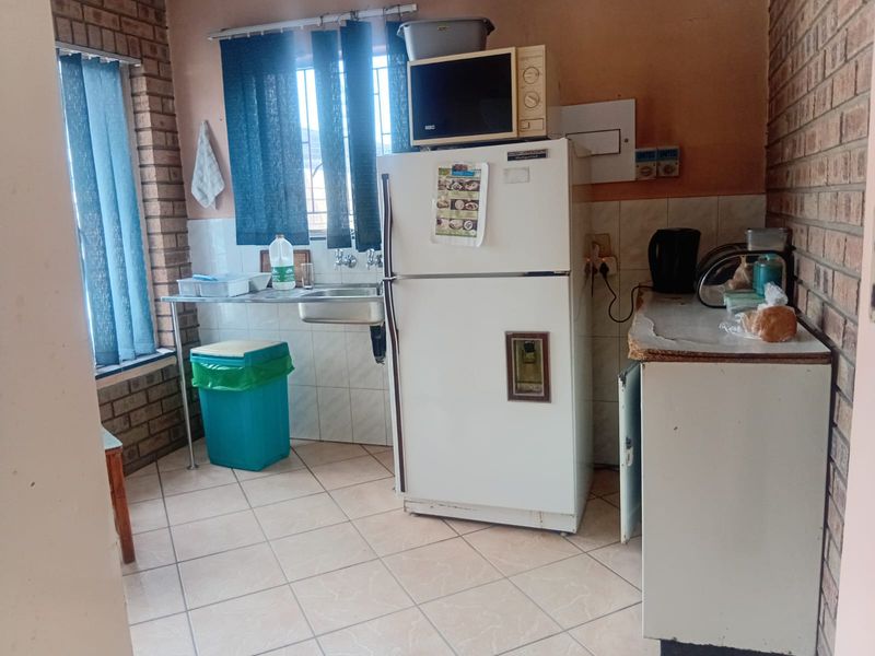 A functional scullery area featuring exposed brick walls, tiled flooring, a stainless steel sink, and a tiled splashback.