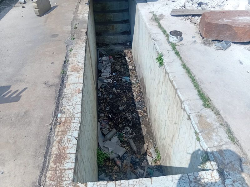 An industrial concrete inspection pit featuring integrated stairs, currently showing significant wear and debris accumulation.