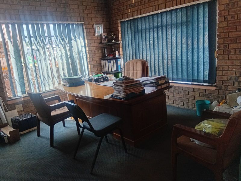 A functional office space featuring exposed brick walls, carpeted flooring, and large windows with vertical blinds.