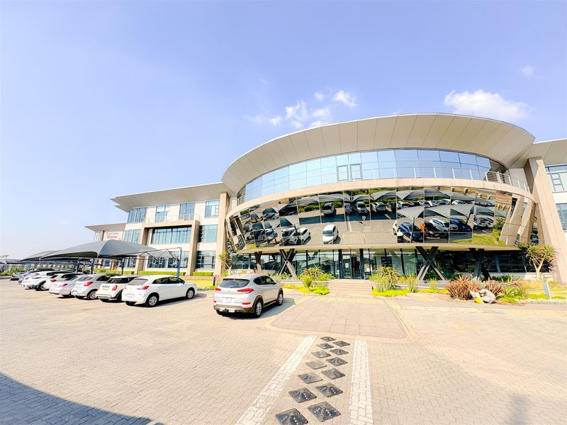 Modern commercial office building featuring a prominent curved glass facade, extensive paved parking area, and integrated shade cloth carports.