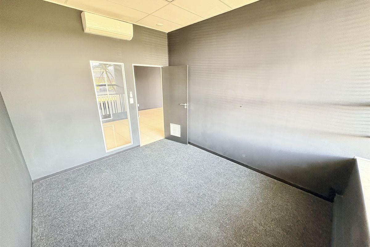 A clean, empty office space featuring grey carpet flooring, a suspended ceiling, and a wall-mounted split-system air conditioner.