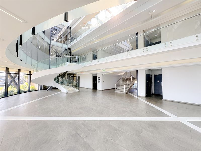 Spacious modern office building atrium featuring a striking spiral staircase, glass balustrades, and abundant natural light from overhead skylights.