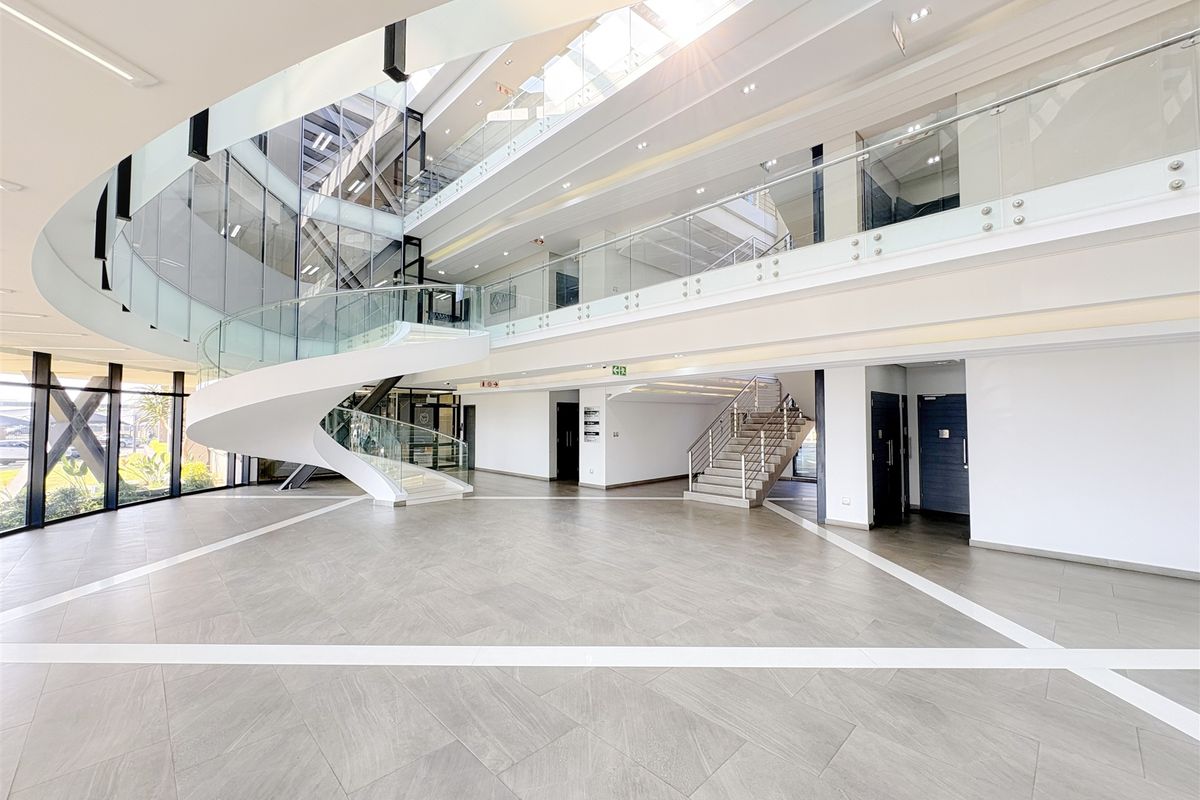 Spacious modern office building atrium featuring a striking spiral staircase, glass balustrades, and abundant natural light from overhead skylights.