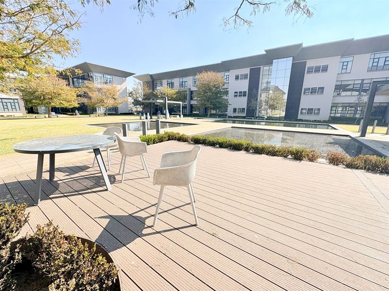 A well-maintained outdoor deck area featuring composite decking, overlooking a landscaped garden with water features and modern commercial office buildings.
