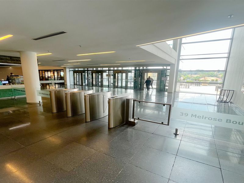 Modern office building lobby featuring secure turnstile access, polished stone flooring, and expansive glass frontage providing natural light and street access.