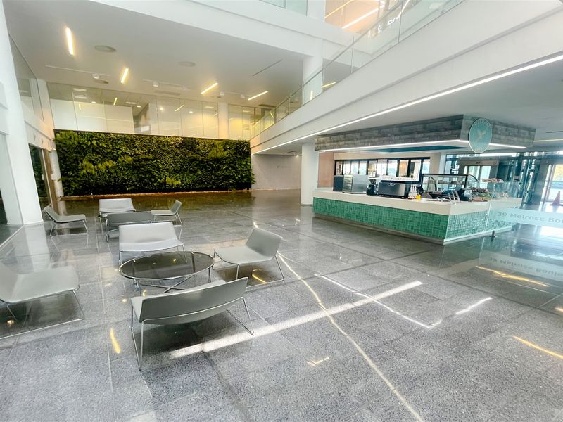 Spacious modern office building lobby featuring a vertical garden wall, polished stone flooring, and a built-in reception or cafe counter area.