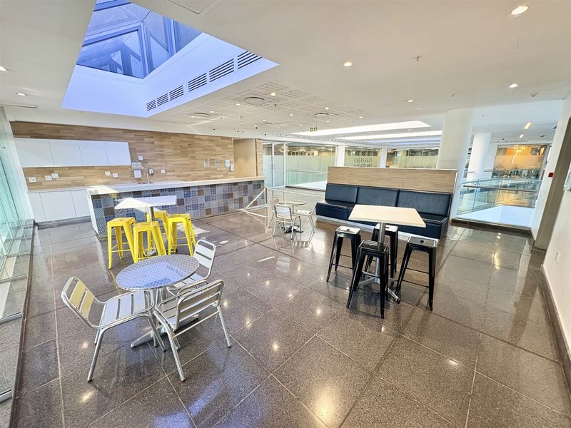 Modern open-plan office break-out area featuring a kitchenette, tiled flooring, and a large skylight providing ample natural light.
