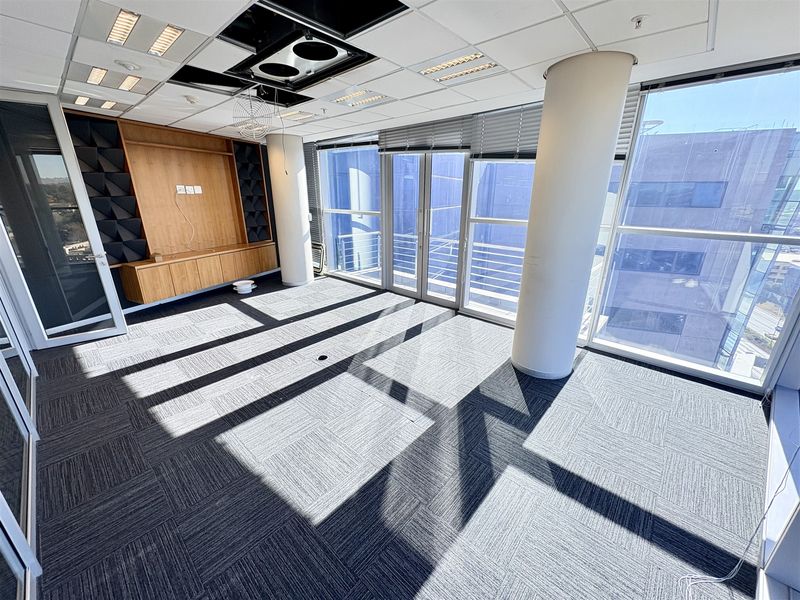 Bright, open-plan office space featuring floor-to-ceiling windows, carpet tiles, built-in cabinetry, and structural columns, offering a professional environment with natural light.