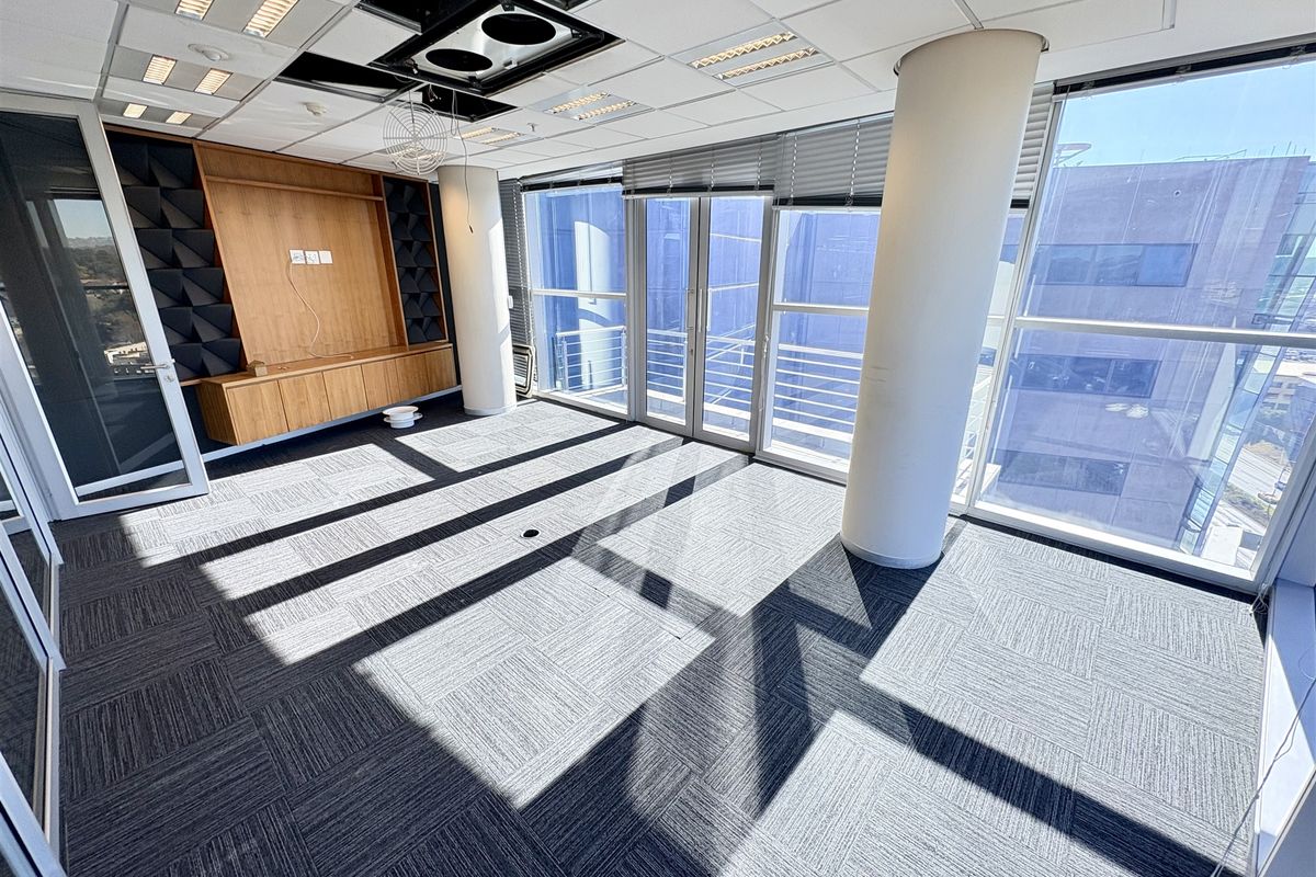 Bright, open-plan office space featuring floor-to-ceiling windows, carpet tiles, built-in cabinetry, and structural columns, offering a professional environment with natural light.