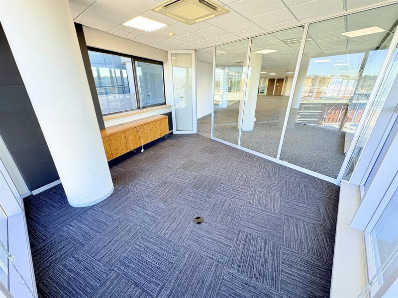 A bright, vacant office space featuring glass partitioning, carpet tiles, a suspended ceiling, and built-in cabinetry, offering a professional and modern work environment.
