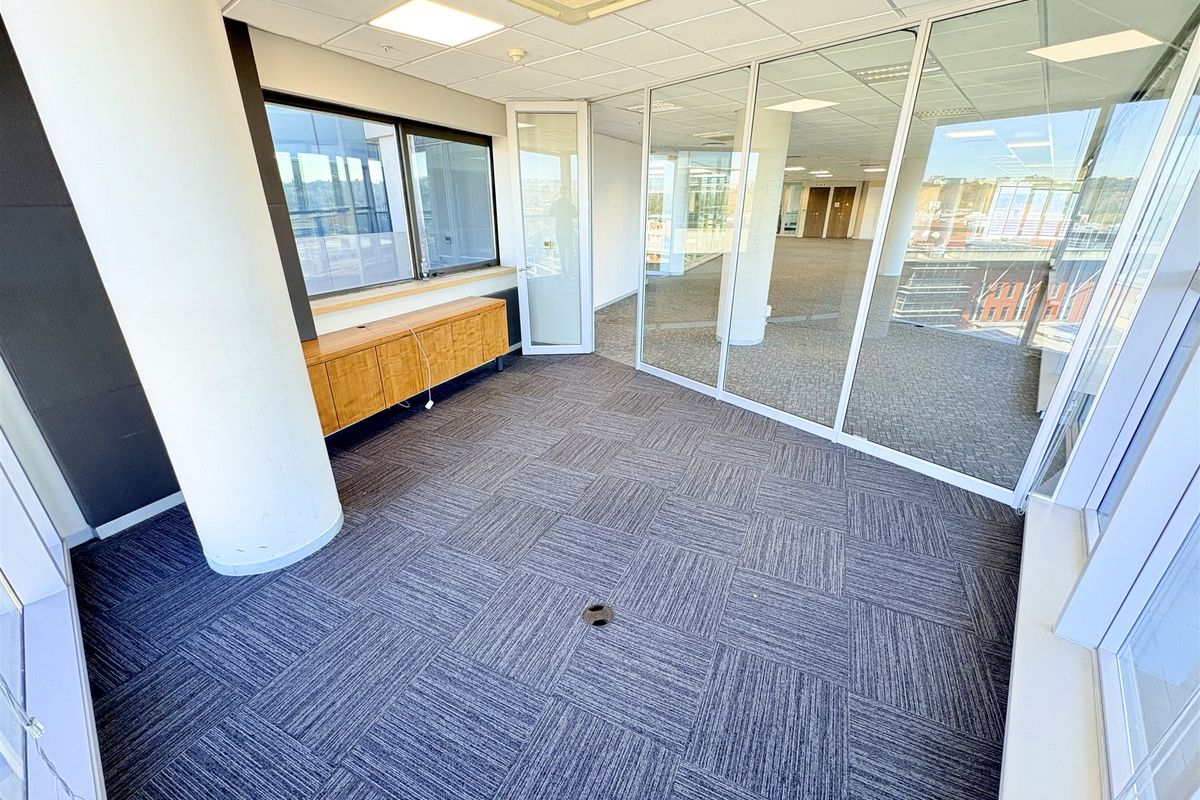 A bright, vacant office space featuring glass partitioning, carpet tiles, a suspended ceiling, and built-in cabinetry, offering a professional and modern work environment.