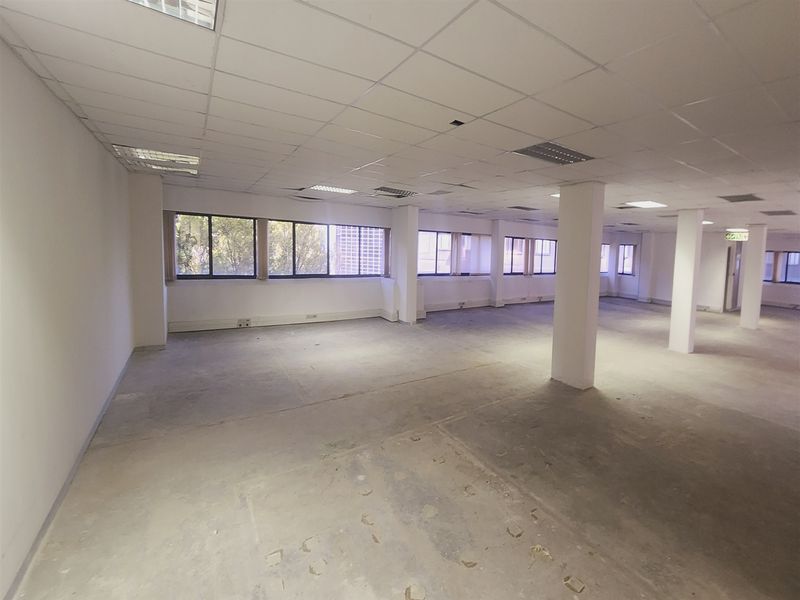 A large, open-plan office space featuring a suspended ceiling, structural columns, and expansive windows, currently in a shell condition awaiting fit-out.