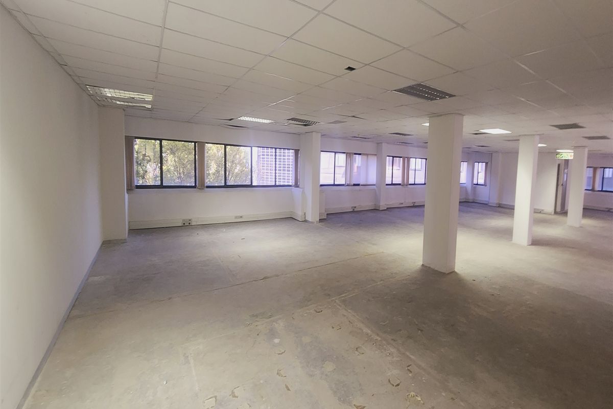 A large, open-plan office space featuring a suspended ceiling, structural columns, and expansive windows, currently in a shell condition awaiting fit-out.